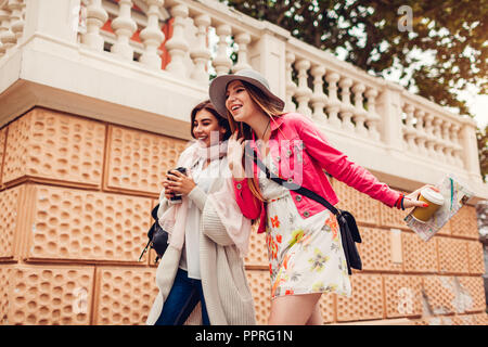 Due donne turisti divertirsi andando sightseeing usando la mappa di Odessa. Happy amici viaggiatori di ridere mentre si cammina e di bere il caffè Foto Stock