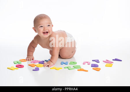 Un ridere di sette mesi di età bambino gioca con alfabeto di schiuma giocattoli. Girato in studio su un bianco, sfondo senza giunture. Foto Stock