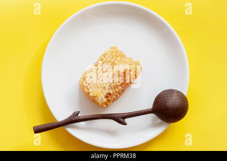 Organici di favi, il cucchiaio di legno nella piastra bianca, sfondo giallo. Gli ingredienti naturali, prodotti apistici per il concetto di cibo Foto Stock