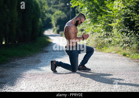 Ritratto di un giovane fisicamente l uomo che mostra il suo ben addestrato corpo - Atletico muscolare Bodybuilder Modello di Fitness in posa all'aperto Foto Stock