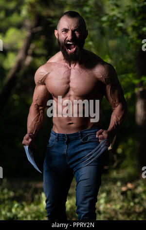 Ritratto di una adatta fisicamente Wolverine con artigli che mostra il suo ben addestrato corpo - Atletico muscolare Bodybuilder supereroe Fitness in posa all'aperto Foto Stock