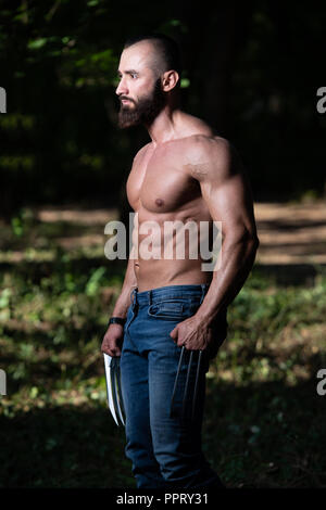 Ritratto di una adatta fisicamente Wolverine con artigli che mostra il suo ben addestrato corpo - Atletico muscolare Bodybuilder supereroe Fitness in posa all'aperto Foto Stock