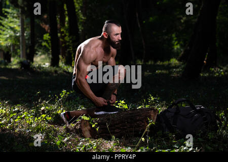 Atleta maschio prepara la legatura lacci delle scarpe nella foresta per la corsa in posizione di parcheggio esterno e fare esercizio Foto Stock