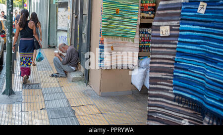 Atene Grecia/Agosto 17, 2018: Donna che cammina verso il basso chiuso il mercato delle pulci con graffiti sulle porte chiuse Foto Stock