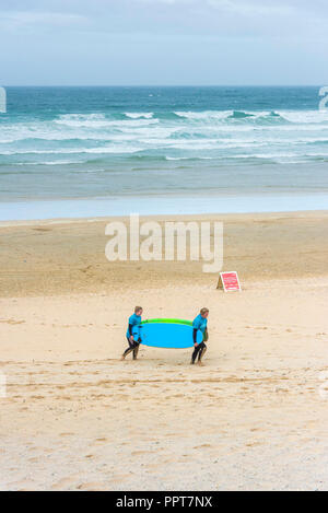 Due turisti che trasportano i loro assunti tavole da surf torna a Fistral Beach Surf School in Newquay in Cornovaglia. Foto Stock