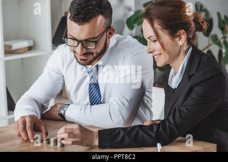 Felice finanzieri impilamento di monete sul tavolo in ufficio Foto Stock