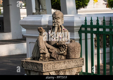 Custode di pietra statua in posizione seduta con una ghirlanda di orchidee, Wat Arun, Bangkok, Thailandia Foto Stock