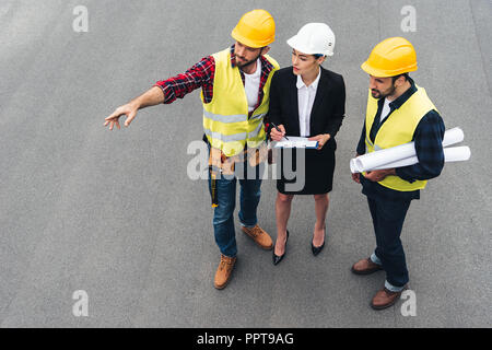 Vista aerea di ingegnere di sesso femminile e di lavoratori di sesso maschile con appunti e progetti rivolti alla costruzione Foto Stock