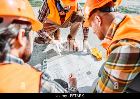 Inquadratura ravvicinata di un gruppo di costruttori di copricapi rigidi aventi conversazione sul piano di costruzione Foto Stock