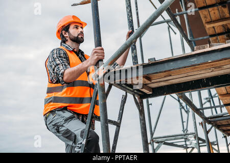 Barbuto builder arrampicate sulle impalcature al sito in costruzione Foto Stock