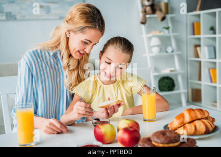 Madre e figlia applicando inceppata sul pane per la colazione a casa Foto Stock