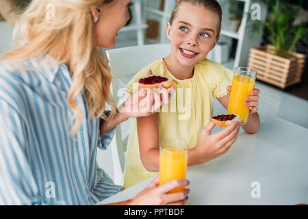 Madre e figlia mangiare baguette con marmellata e succo d'arancia a casa Foto Stock