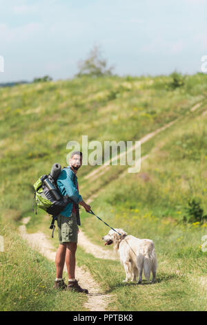 Viaggiatore a piedi con il golden retriever cane sul percorso sul campo estivo Foto Stock