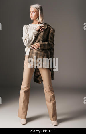 Elegante elegante modello in posa di autunno maglione beige, pantaloni e giacca di tweed, su grigio Foto Stock