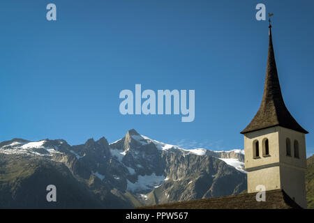 Guardando alla clocktower della chiesa di Bellwald contro lo sfondo delle montagne enormi del Fischertal (Vallese, Svizzera) Foto Stock