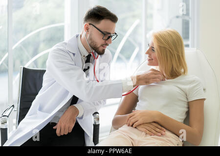 Uomo caucasico medico heartbeat di ascolto della giovane donna paziente con stetoscopio per health check in ospedale. Foto Stock