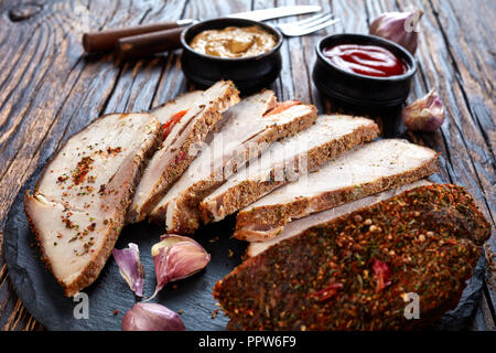 In vecchio stile di prosciutto cotto al forno ripiene con la carota rivestita con spezie, tagliate a fette e servite con ketchup e senape, su uno sfondo di legno, stile rustico Foto Stock