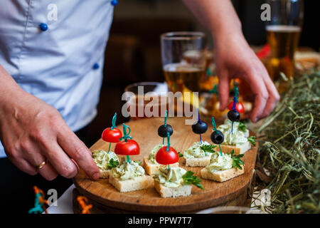 Deliziosi spuntini per la birra. Crostini di fresco con pomodori, olive verdi su pane bianco sul tavolo. Foto Stock