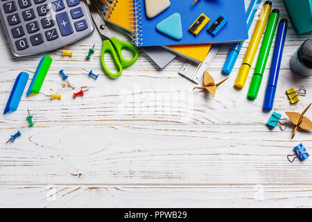 Su un tavolo bianco in un ordine caotico giacciono: calcolatrice, elastico, clip di carta. Si torna a scuola dello sfondo. Foto Stock