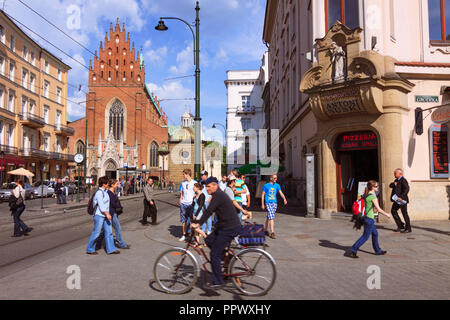 Cracovia in Polonia : la gente a piedi e in bicicletta in Grodzka Street, nell'Unesco di cui la città vecchia. Chiesa della Santa Trinità in background. Foto Stock