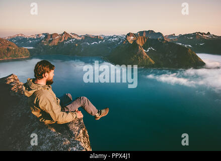 Uomo seduto turistica solo sul bordo della scogliera montagne sopra mare viaggi avventura estrema lifestyle vacanze in Norvegia Foto Stock