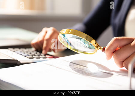 Close-up di una imprenditrice la mano esaminando fattura attraverso la lente di ingrandimento Foto Stock