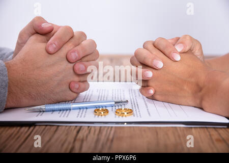 Accoppiare la mano con il divorzio accordo e Golden gli anelli di nozze sulla scrivania in legno Foto Stock