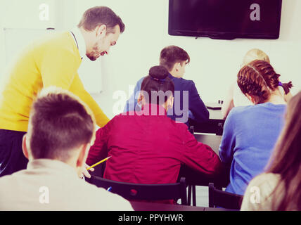 Maestro sorridente dare spiegazione agli studenti durante il lavoro di revisione in classe Foto Stock