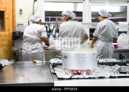 Cottura a vapore pentola in argento con tre lavoratori cucina indossando grembiuli come sfondo Foto Stock