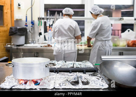 Argento per la cottura a vapore di pentola e padella con due lavoratori cucina indossando grembiuli come sfondo Foto Stock