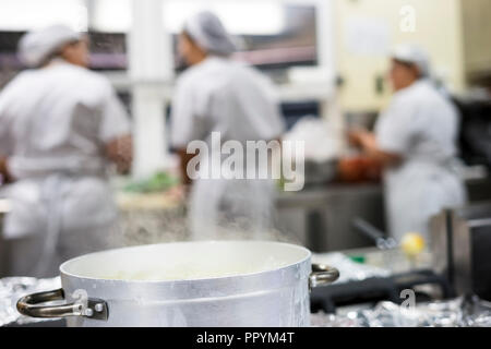 Cottura a vapore pentola in argento con tre lavoratori cucina indossando grembiuli come sfondo Foto Stock