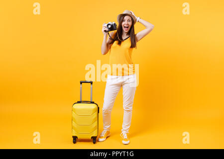 Excited donna turistica in estate abiti casual, cappello con la valigia, retro vintage foto fotocamera isolato su sfondo giallo. Donne in viaggio all'estero t Foto Stock