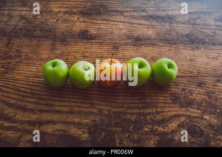 Un unico red apple tra gli altri quelli di colore verde sul tavolo di legno, concetto di scegliere i migliori prodotti Foto Stock