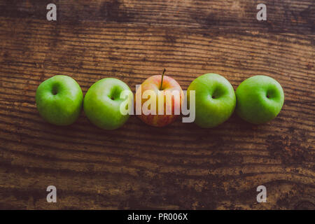 Un unico red apple tra gli altri quelli di colore verde sul tavolo di legno, concetto di scegliere i migliori prodotti Foto Stock