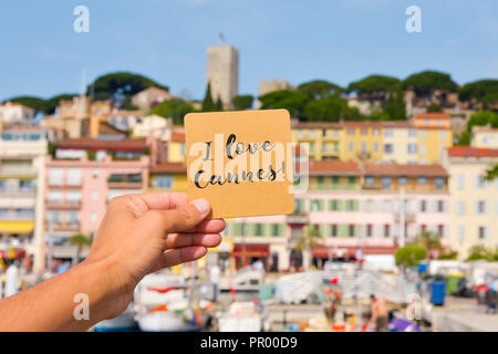 Primo piano di un giovane uomo caucasico tenendo un cartello marrone con il testo io amo Cannes scritto in esso, in Vieux Port, il vecchio porto di Cannes, Franc Foto Stock