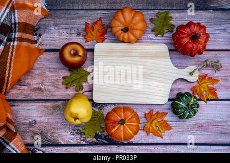 Accogliente autunno autunno concetto con tagliere in legno per una copia dello spazio, circondato da zucche e zucche. Plaid coperte e uno sfondo di legno Foto Stock
