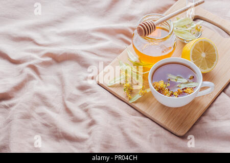 Tè con Linden, miele e limone. Il vassoio sul letto, il concetto di trattamento di raffreddori Foto Stock