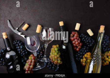 Wineglasses con vino rosso e bianco, bottiglie, uva, corkcrew e tappi giacente sul legno scuro dello sfondo. Vista dall'alto. Lay piatto. Spazio di copia Foto Stock