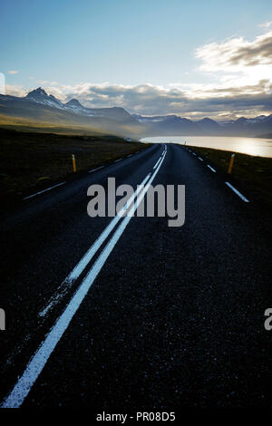 Un vuoto che la strada con linee bianche taglio attraverso l'est il paesaggio dei fiordi di Islanda. Foto Stock