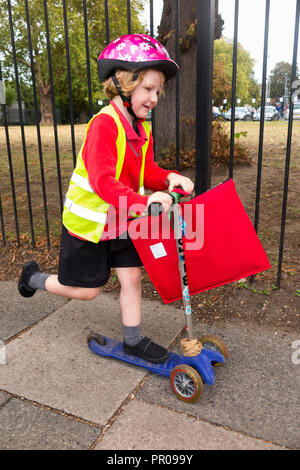 Bambino di 4 anni su scooter / ragazza la hi vis / alta visibilità giacca giubbotto di scooter a casa dalla scuola di classe di ricezione. Regno Unito. (102) Foto Stock