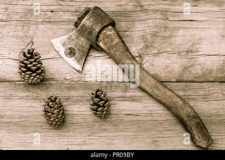 Vecchio strumento su sfondo di legno. Vecchio colorate ax e pigne sulla vecchia superficie di legno. In stile vintage Foto Stock