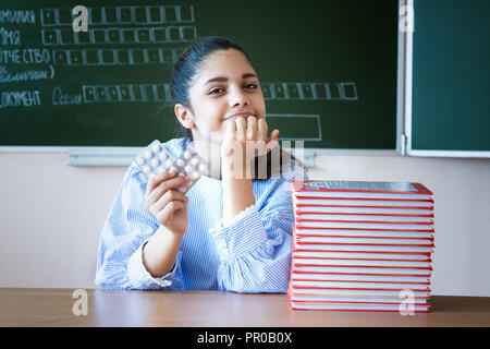 Studente sorridente con piils si siede vicino a lavagna in aula Foto Stock