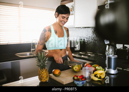 Donna sorridente il taglio di frutti in cucina e la registrazione su video. Giovane donna in cucina il contenuto di registrazione per videoblog. Foto Stock