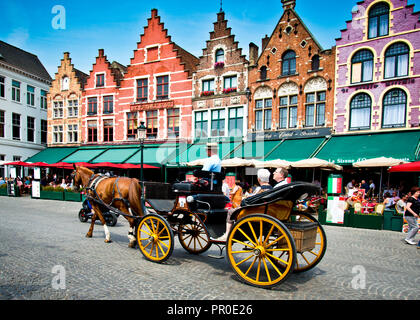 I turisti che vengono portati in giro della città in una carrozza trainata da cavalli passando vecchi edifici ora caffè e ristoranti con le galle ornate nella storica Brugge, Foto Stock