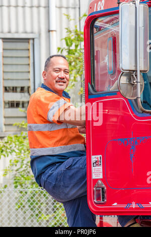 Un felice il samoano camionista in indumenti ad alta visibilità, arrampicata in una cabina di un rosso semi rimorchio prime mover carrello Foto Stock