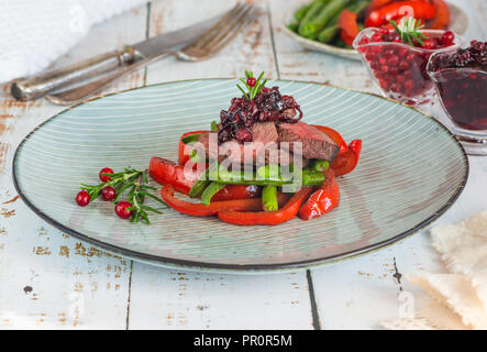 Fette di Bistecca di cervo con salsa di lingonberry, arrostire i peperoni e i fagiolini verdi Foto Stock