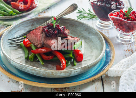Fette di Bistecca di cervo con salsa di lingonberry, arrostire i peperoni e i fagiolini verdi Foto Stock