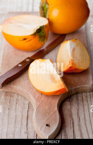 Persimmons mature e coltello sulla tavola di legno Foto Stock