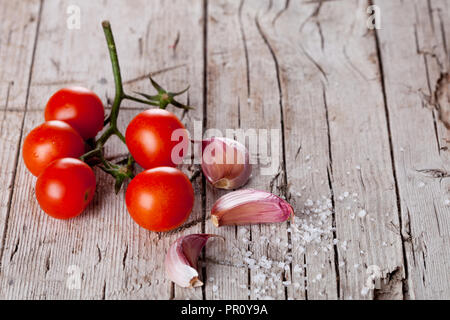 Pomodori ciliegini, aglio, pepe e sale in stile rustico sfondo di legno Foto Stock