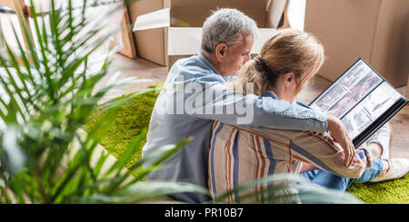 Angolo di alta vista della coppia senior guardando album di foto durante il trasferimento nella nuova casa Foto Stock